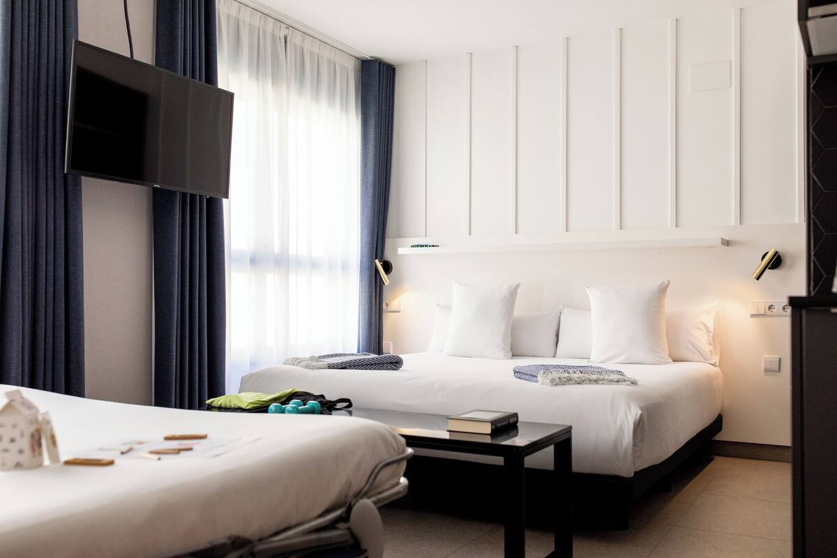 Habitación de hotel con cama, mesita de noche y televisor de pantalla plana montado en la pared.