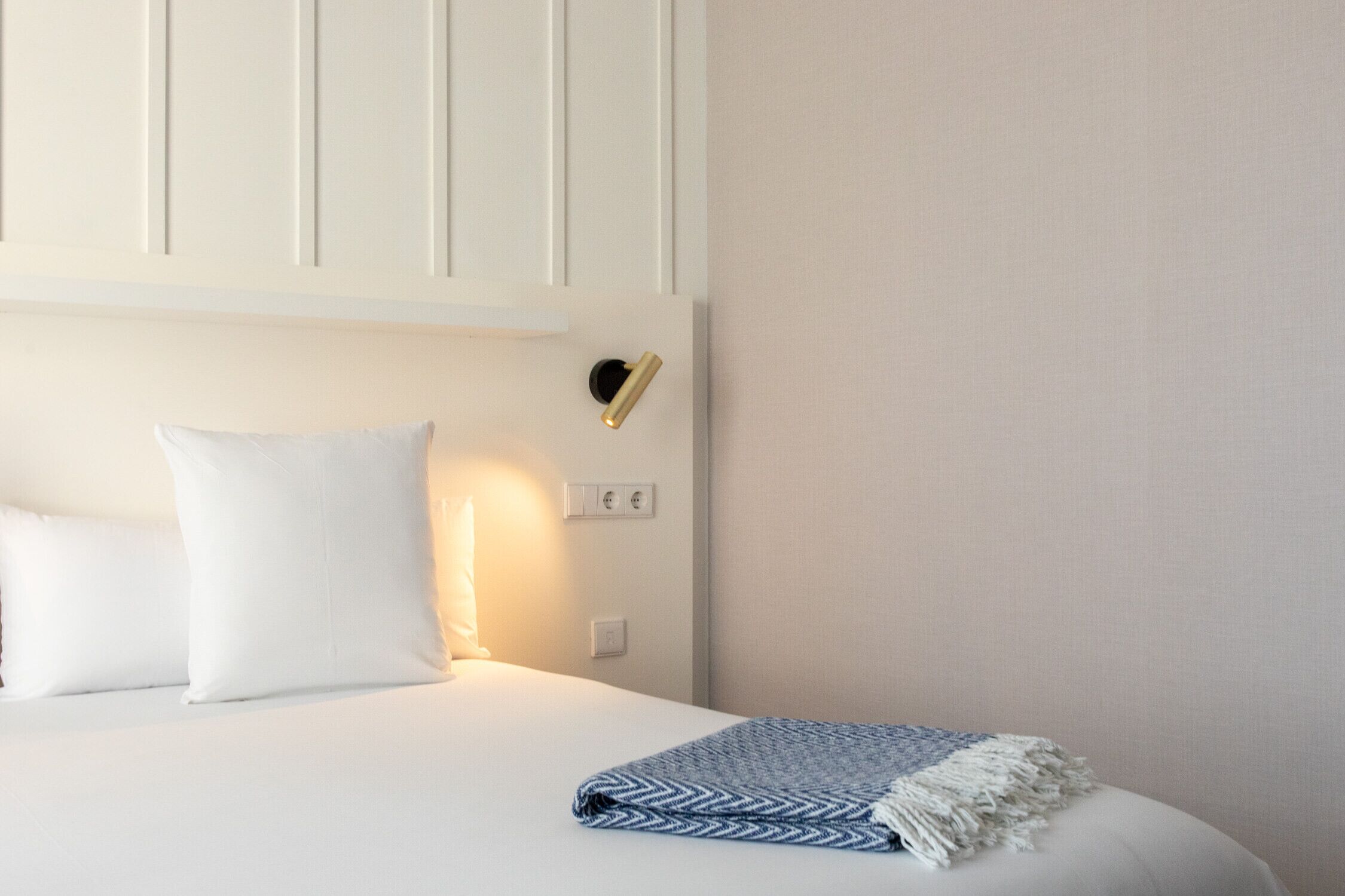 A neatly made bed with white linens and a blue and white patterned throw blanket.