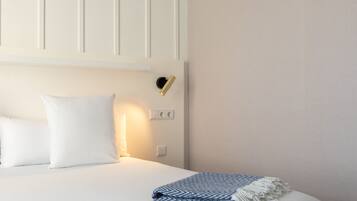 A neatly made bed with white linens and a blue and white patterned throw blanket.