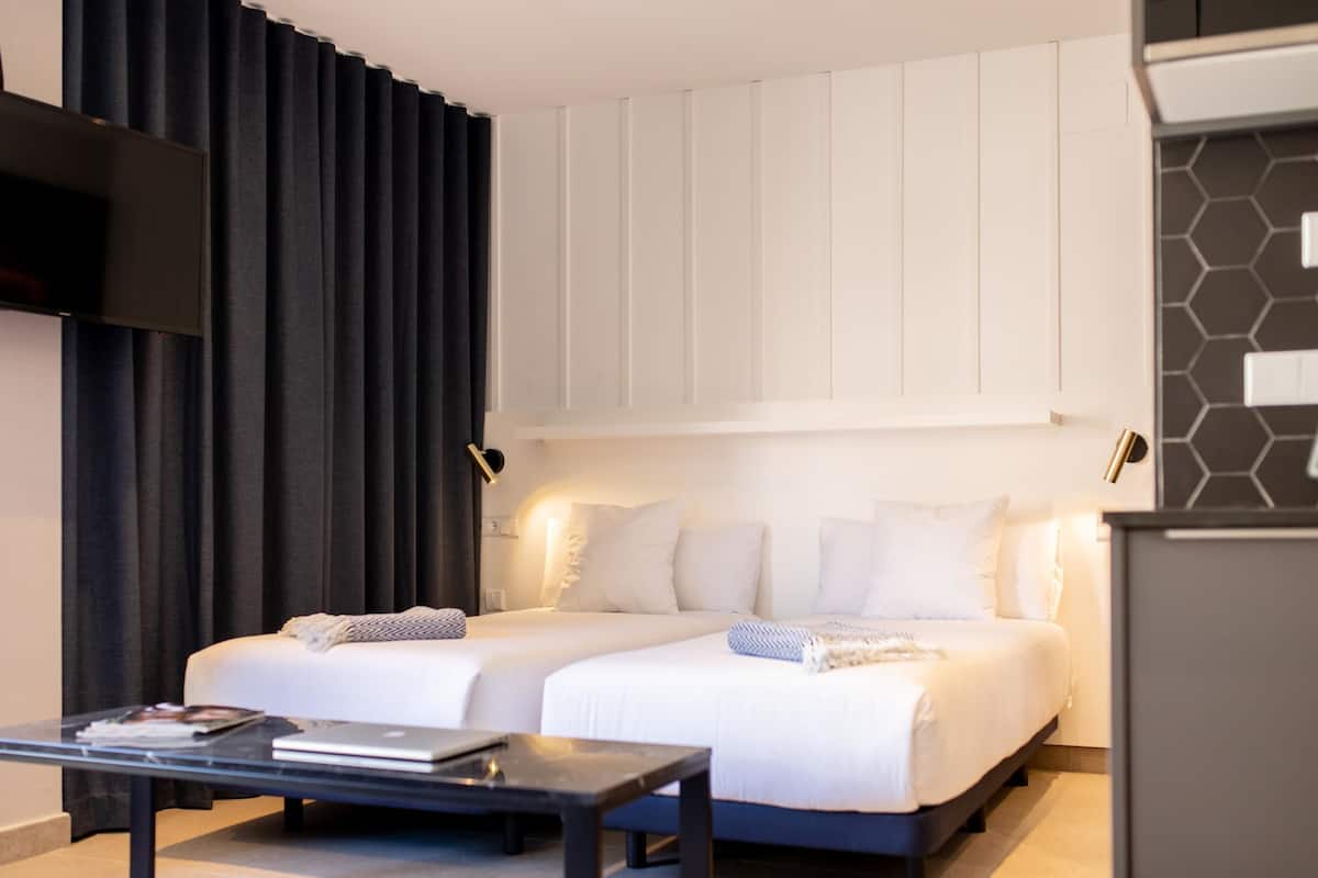 Una habitación de hotel moderna con dos camas, un televisor de pantalla plana, una mesa de centro y un ventanal con cortinas.