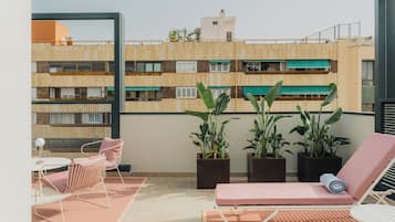 Un balcón con una silla de descanso, una mesita y plantas en macetas.
