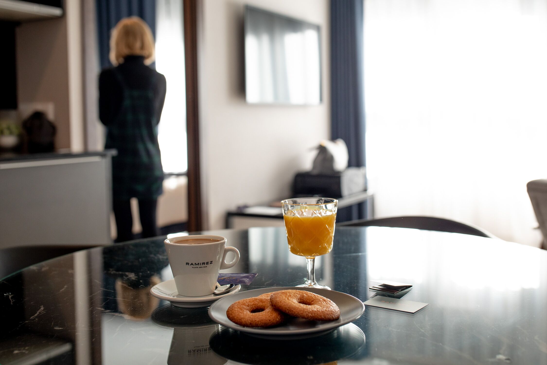 A hotel room with a glass table featuring a cup of coffee, a glass of orange juice, and two donuts.