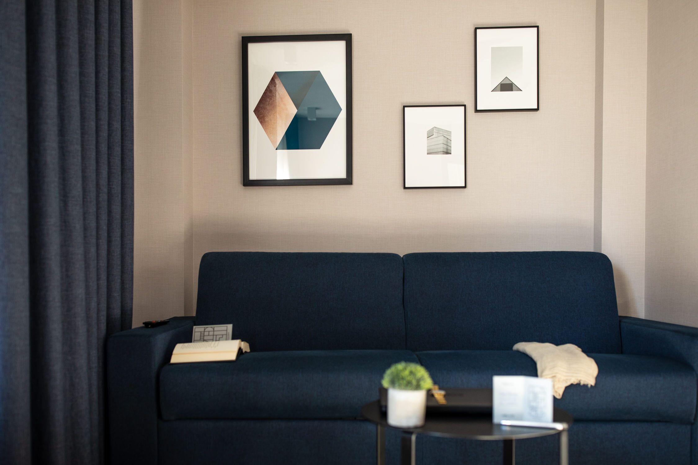 Un canapé bleu foncé, avec une petite table et une plante en pot devant. Trois tableaux encadrés sont accrochés au mur.