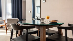 Un coin repas moderne avec une table ronde en verre, quatre chaises noires, une tasse de café et un verre de jus d’orange.