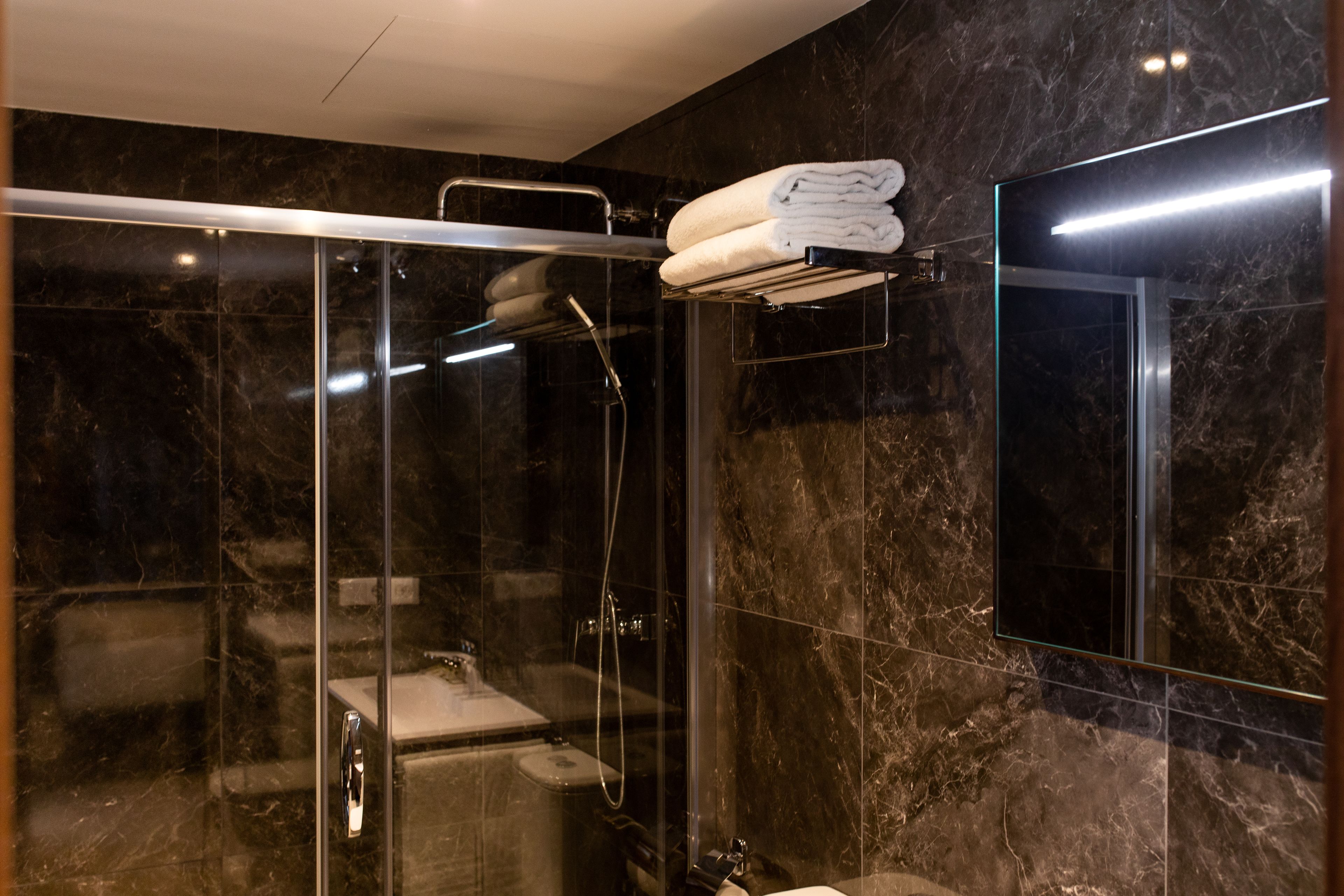A modern bathroom with a glass-enclosed shower, a glass-enclosed toilet, and a towel rack with folded towels.