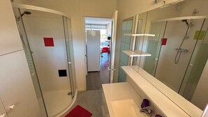 A modern bathroom with a glass shower enclosure, a white sink with a mirror, and a red bath mat.