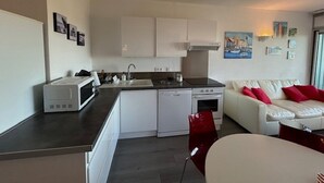 A compact living space with a kitchenette, a white sofa with red cushions, and a dining area.