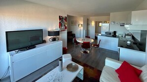 A modern living room with a flat-screen TV, a white sofa, and a dining area with a red table and chairs.