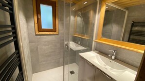 Een moderne badkamer met een glazen douchecabine, een raam met houten kozijn en een witte wasbak.