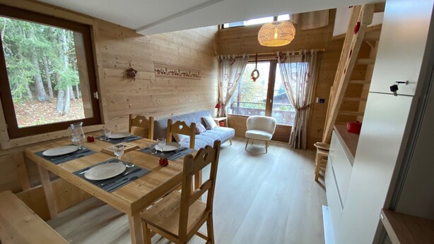Een houten interieur met een eettafel voor vier personen, een bank, een stoel en een trap.