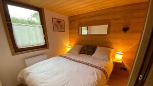 Een gezellig houten slaapkamer met een groot bed, twee bedlampjes, een raam met een gordijn met hartjespatroon, en een ingelijst embleem aan de muur.