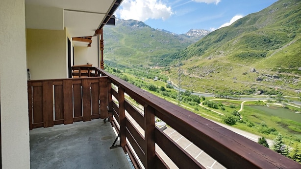Un balcon doté d’une balustrade en bois, donnant sur une vallée avec des montagnes en arrière-plan.