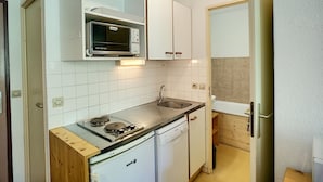 Une cuisine de taille réduite, avec des meubles blancs, un four à micro-ondes, une cuisinière et un lave-vaisselle.