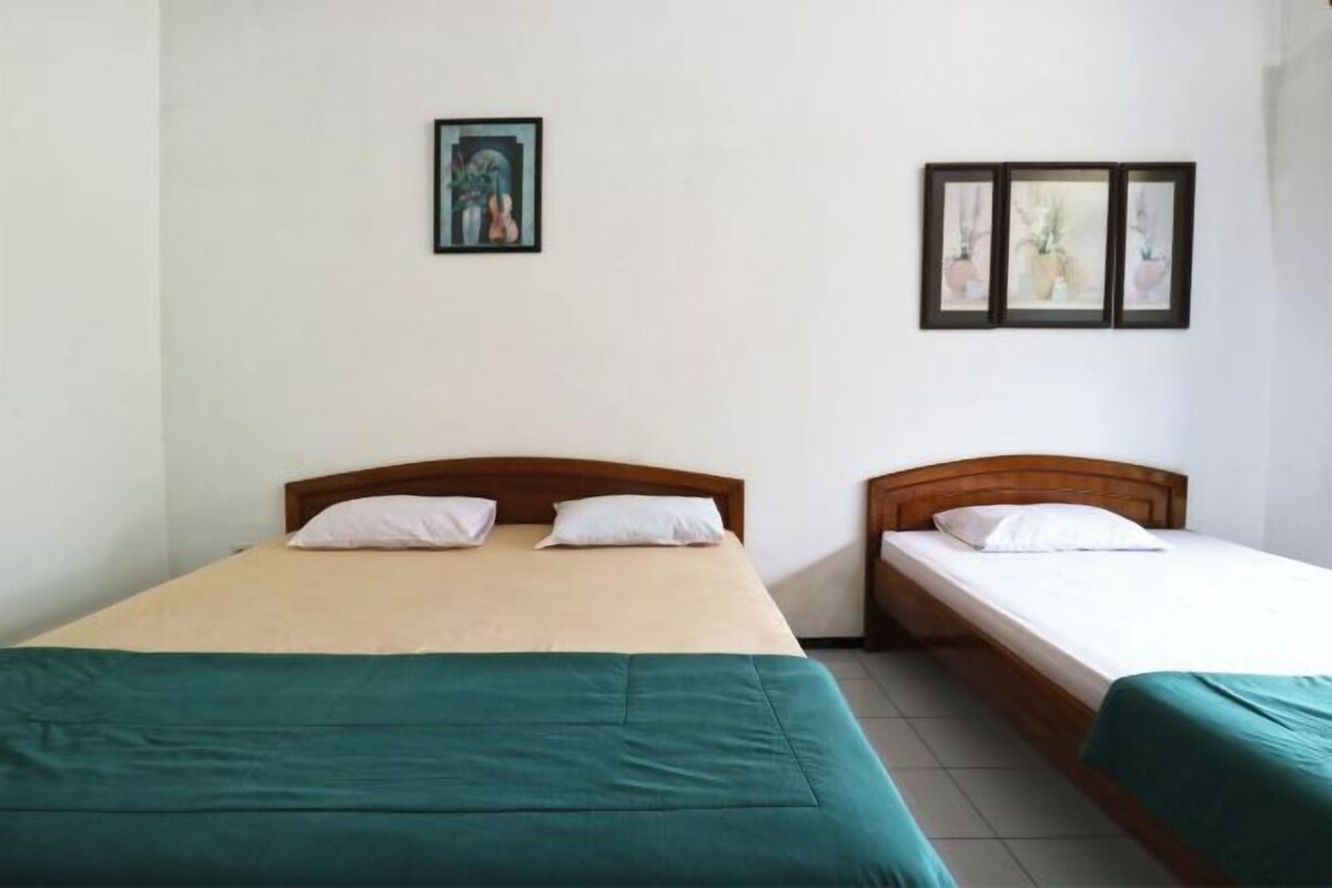 A room with two single beds, each with a wooden headboard and a green bedspread. There are framed pictures on the wall above the beds.