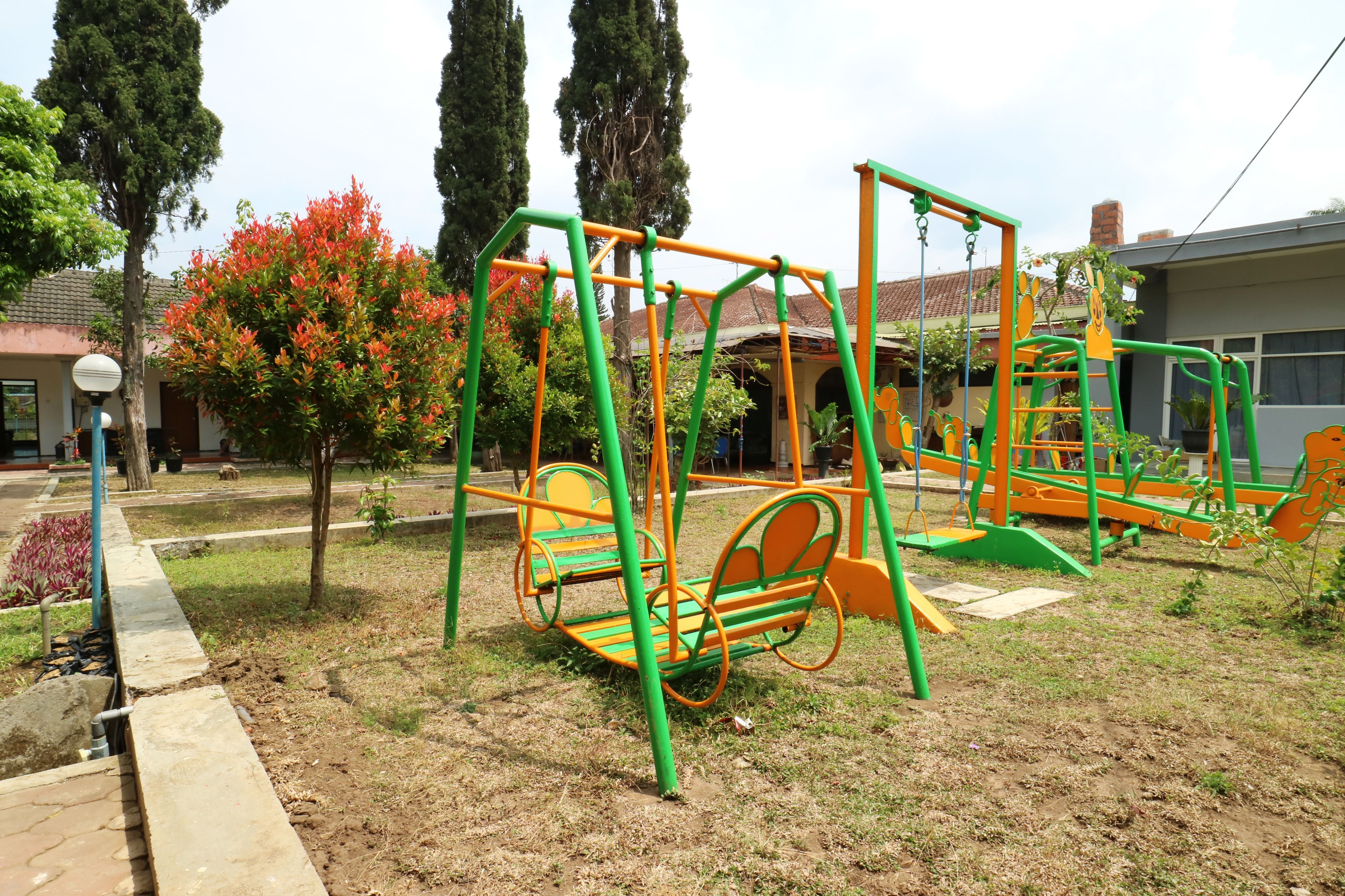 A playground with swings and climbing structures, surrounded by trees and a building in the background.