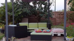 An outdoor seating area with a green sofa and cushions, a white bench, and a wooden pathway. - Chambre Rose Blanche (Le Lude)