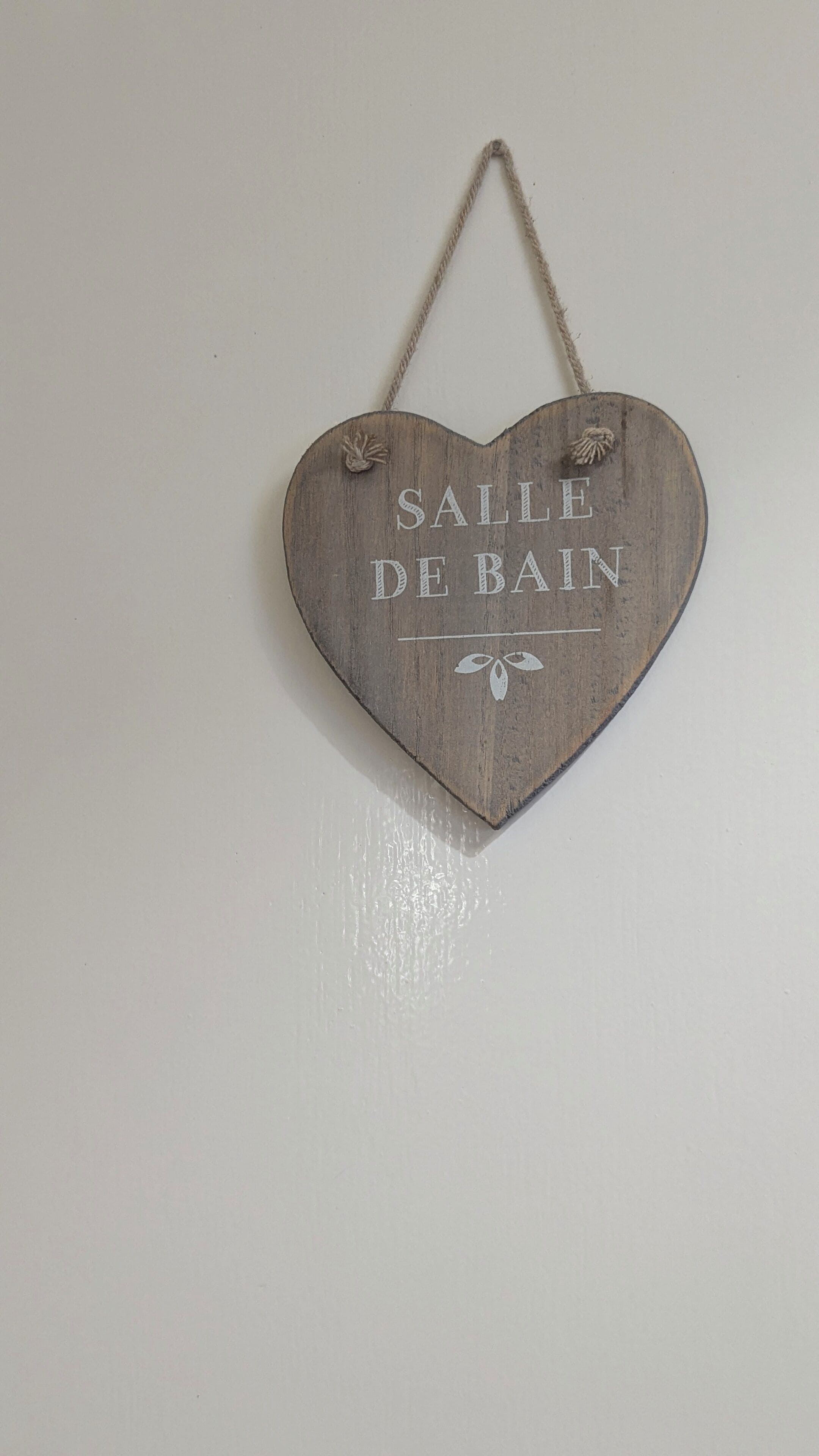 Un letrero de madera con forma de corazón que dice 'SALLE DE BAIN' colgado en una pared.