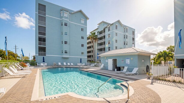A swimming pool with lounge chairs and a building with multiple balconies.