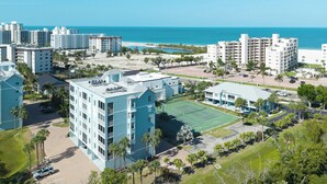 A coastal hotel with multiple buildings, a tennis court, and a beach view.