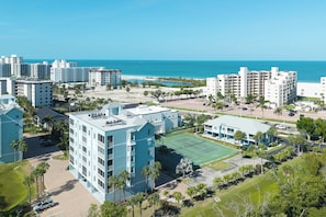 Un hotel costero con varias edificaciones, una cancha de tenis y vista a la playa.
