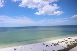 A beach with clear turquoise water, a sandy shore, and a few beach umbrellas. - Relax In The Sunshine! Lovely 2B/2B Vacation Condo w/ All Weather Lanai, Walk To Beach, Resort Pool! (Fort Myers Beach)