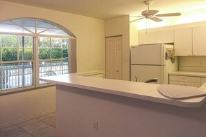 A kitchen with a large window, a ceiling fan, and a refrigerator. - Relax In The Sunshine! Lovely 2B/2B Vacation Condo w/ All Weather Lanai, Walk To Beach, Resort Pool! (Fort Myers Beach)