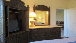 A bedroom with a large bed, a dresser with a mirror, a television, and a lamp.