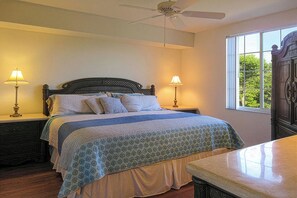 A bedroom with a bed, two bedside lamps, a ceiling fan, and a window with a view of greenery. - Relax In The Sunshine! Lovely 2B/2B Vacation Condo w/ All Weather Lanai, Walk To Beach, Resort Pool! (Fort Myers Beach)