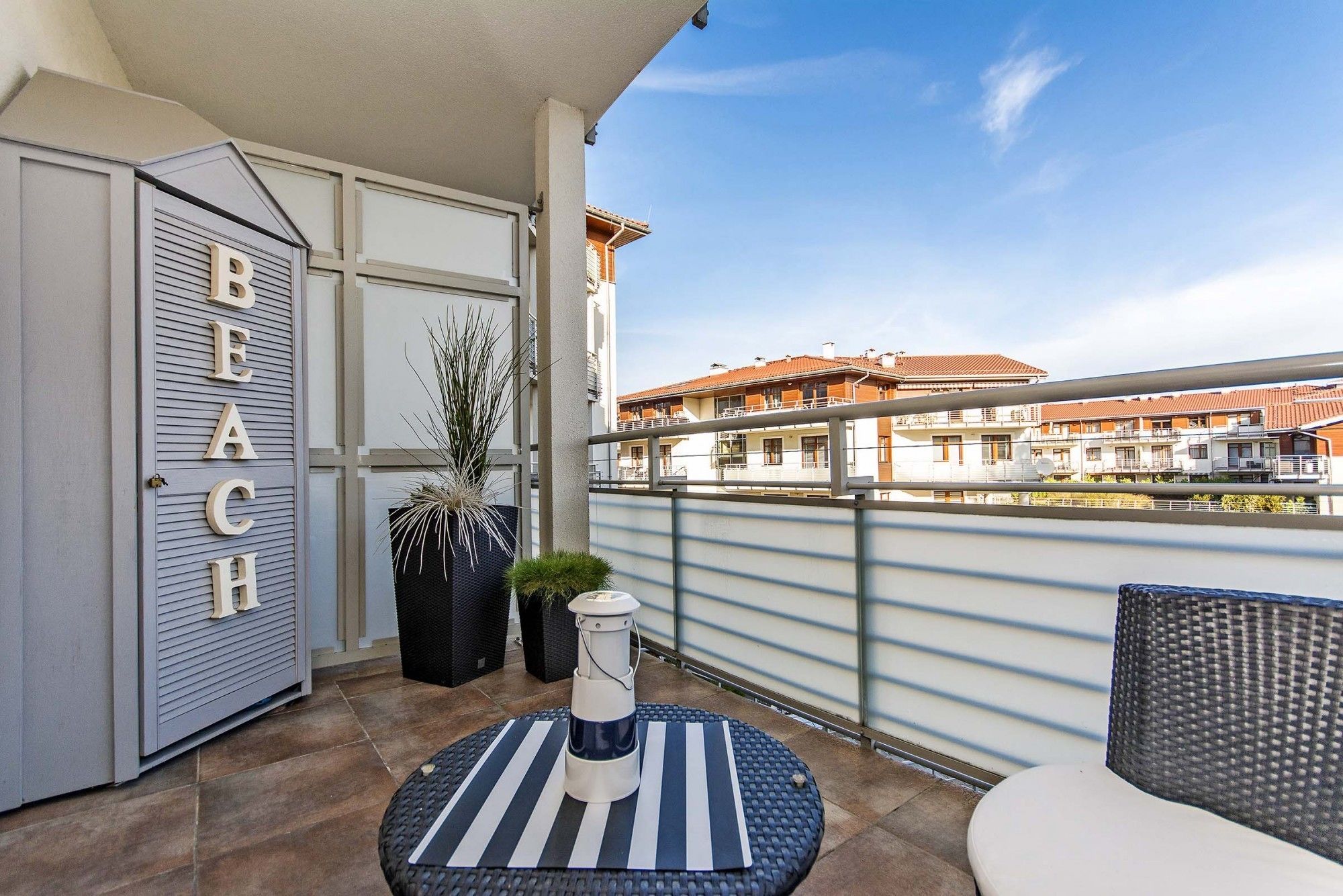 Un balcón con un letrero que dice 'BEACH', muebles de exterior y vistas a edificios residenciales.