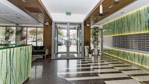 Una hall moderna con scrivania della reception, area salotto e parete con un motivo verde originale.