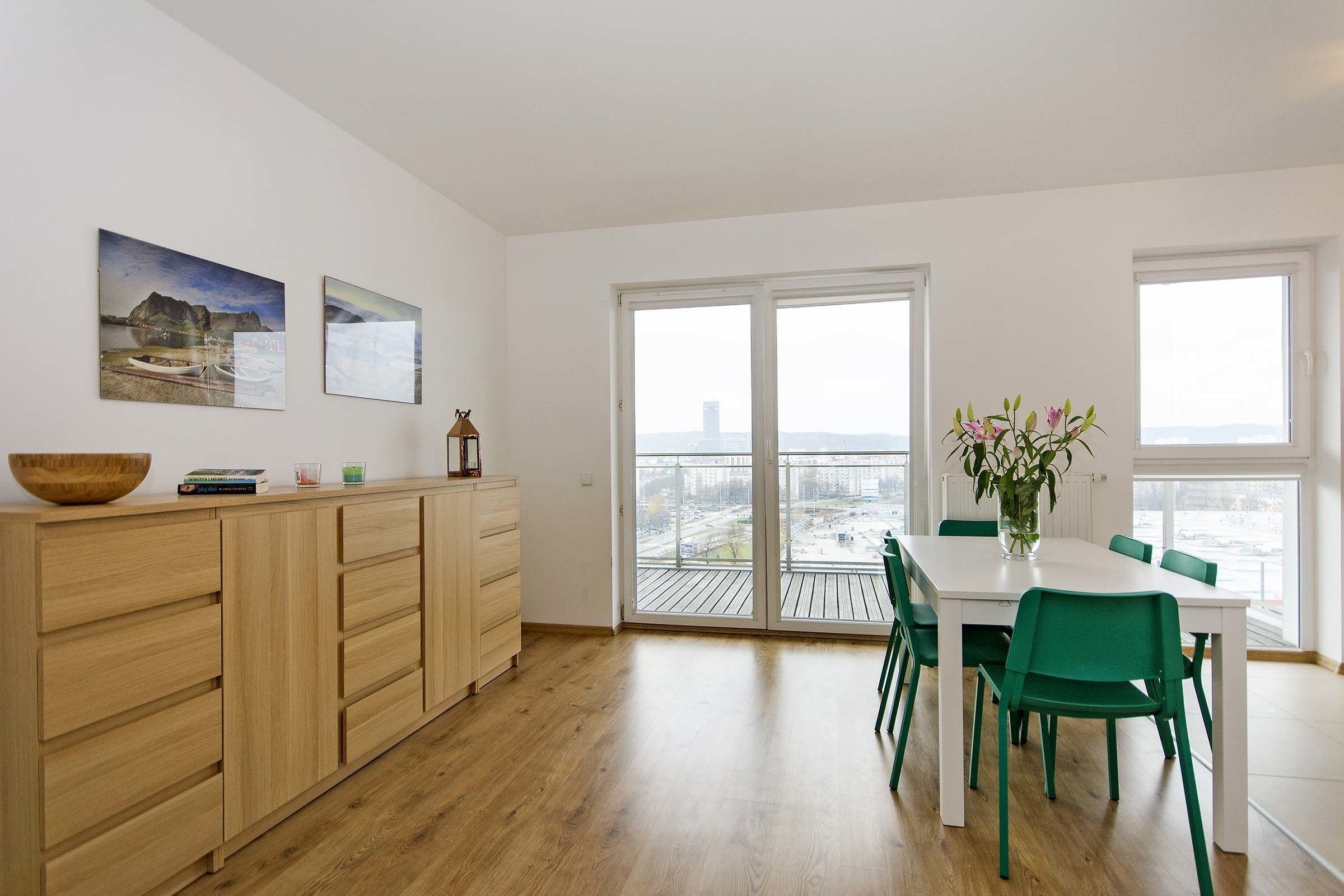 Una cocina moderna con armarios de madera, una mesa de comedor con sillas verdes y un ventanal con vista a la ciudad.