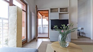 Un soggiorno moderno con un'ampia finestra, un divano, un tavolino da caffè con un vaso e una televisione su un mobile bianco.