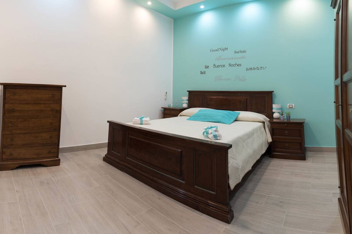 A bedroom with a wooden bed, a nightstand, a dresser, and a wall with multilingual "Good Night" text.