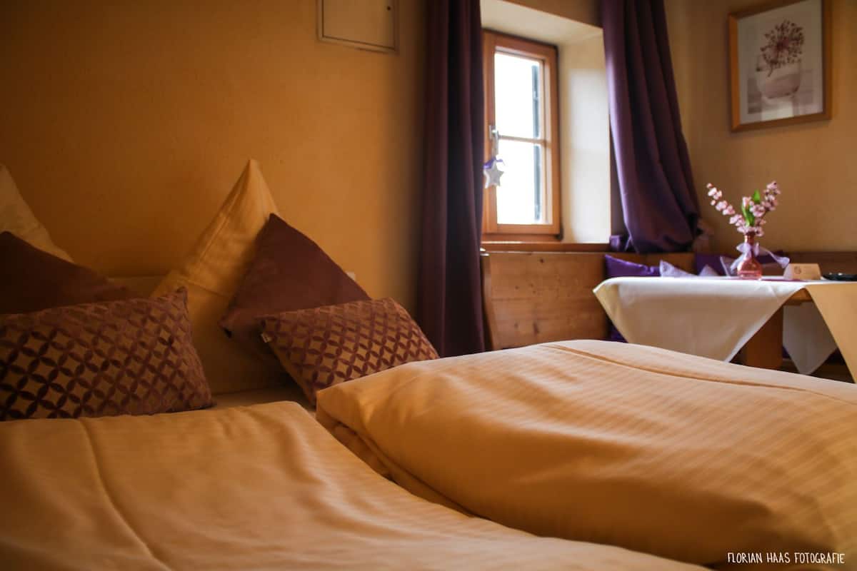 A hotel room with two beds, a wooden dresser, a window with curtains, and a table with a vase of flowers.