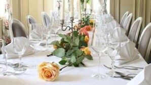 Een formele eetzaal met een lange tafel gedekt voor een maaltijd, met bloemen gordijnen en kandelaars.