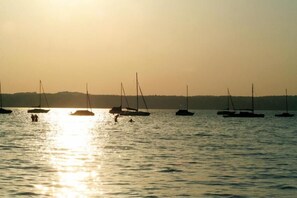 A sunset over a calm body of water with several sailboats anchored.