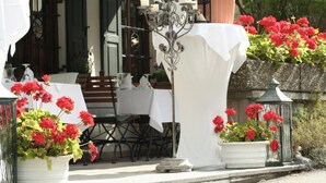 Een terras met een eettafel, omringd door rode geraniums in potten.