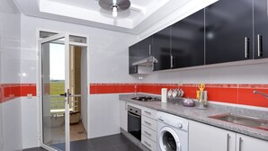 Une cuisine moderne avec des meubles blancs et noirs, un lave-linge encastré et un dosseret de carrelage rouge.