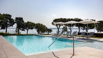 A swimming pool with lounge chairs and umbrellas, surrounded by trees and a view of the water.