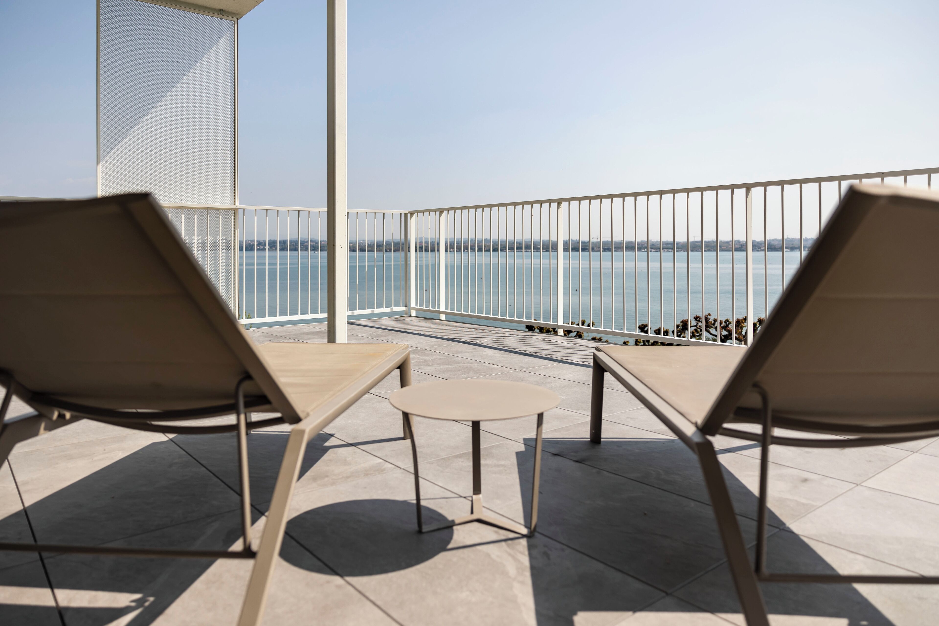 Un balcone con due poltrone e un tavolino, vista su un corpo d'acqua.