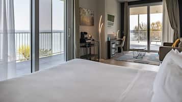 A hotel room with a large bed, a desk with a chair, a small table, and a balcony with a railing.