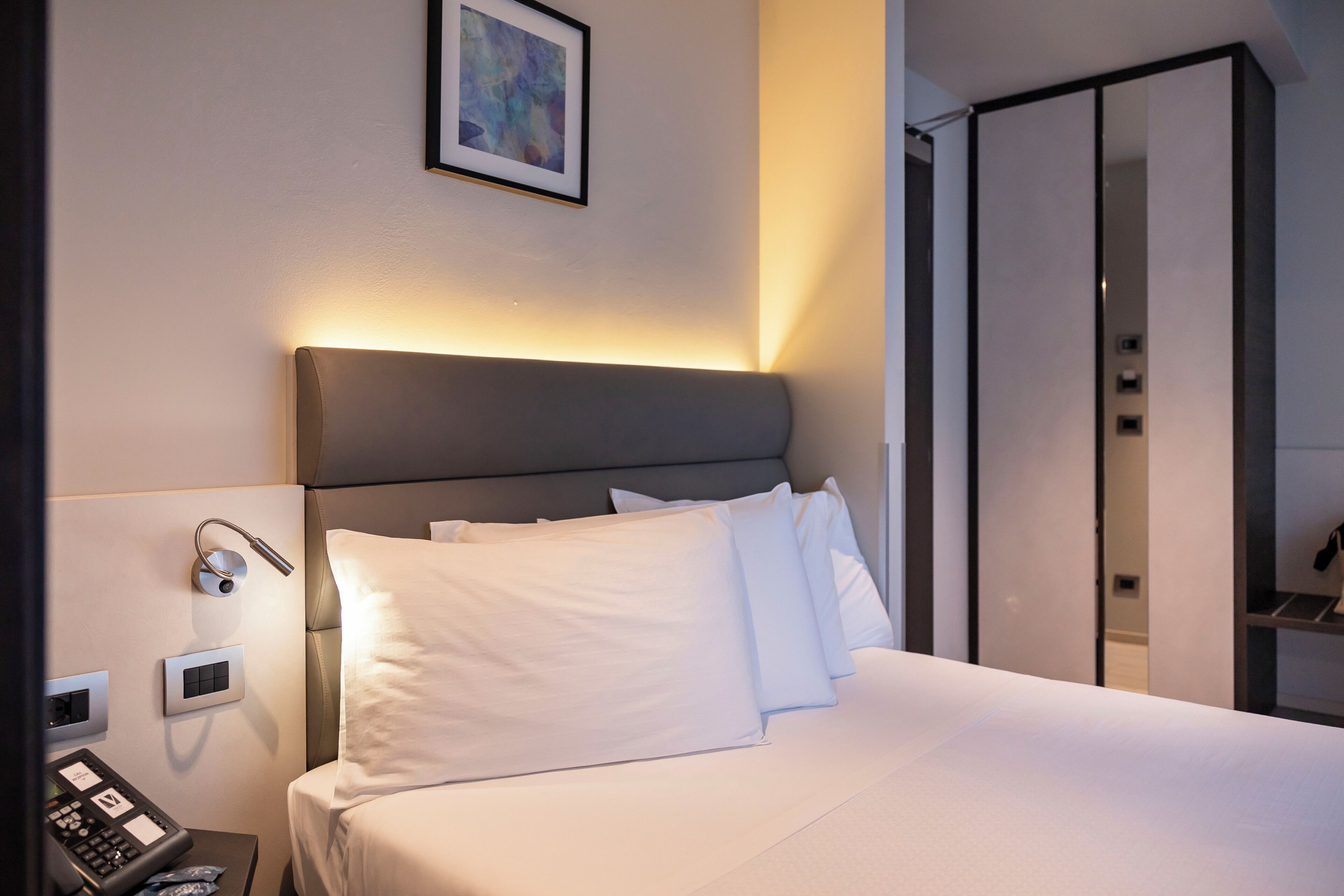 A hotel room with a bed, bedside controls, a phone, and a wardrobe.
