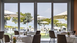 An indoor dining area with large windows, tables set for dining, and umbrellas providing shade. - Vision Hotel (Peschiera del Garda)