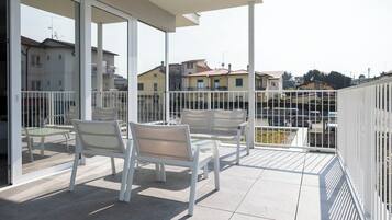 Un balcon avec des chaises blanches et une table, une porte vitrée et une vue sur des immeubles résidentiels.