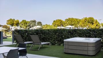 Un espacio al aire libre con un jacuzzi, sillones de descanso y sombrillas.
