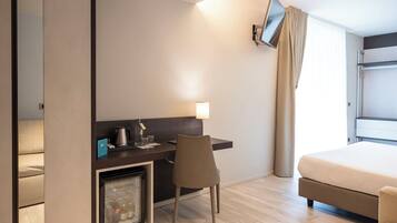 Ein Hotelzimmer mit Bett, Schreibtisch und Stuhl, kleinem Kühlschrank, Wand-Fernseher und einem Fenster mit Vorhängen.