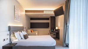 A modern hotel room with a large bed, a desk, a chair, and a flat-screen TV. - Vision Hotel (Peschiera del Garda)