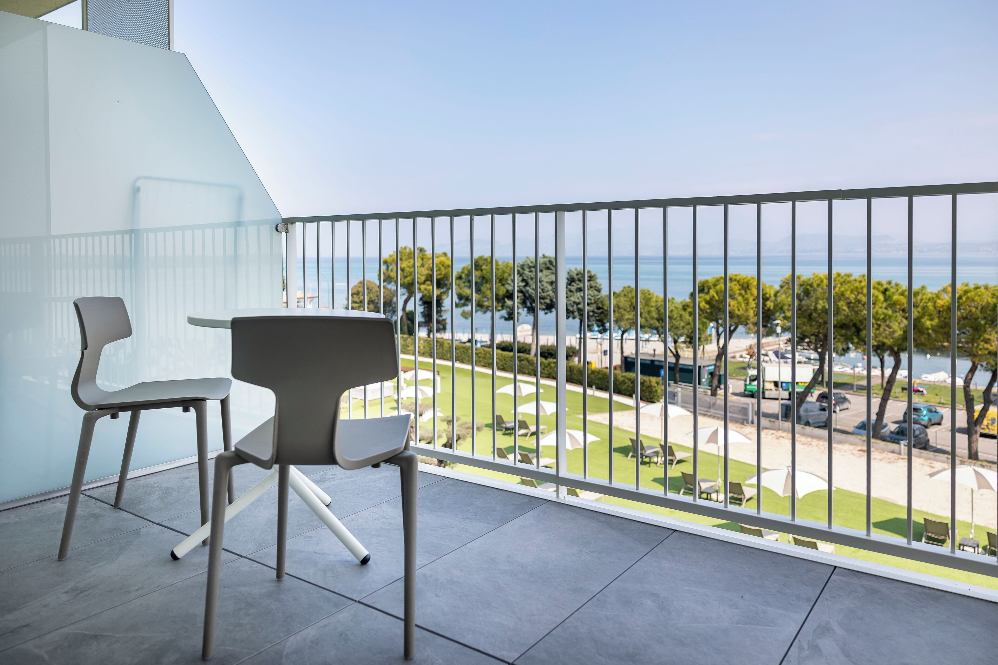 A balcony with two chairs and a table, overlooking a beach and trees.