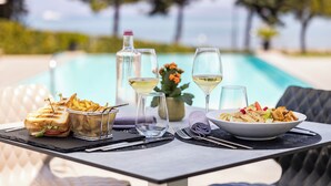 A dining table with a sandwich, a bowl of salad, and a bottle of water, set against a poolside view. - Vision Hotel (Peschiera del Garda)
