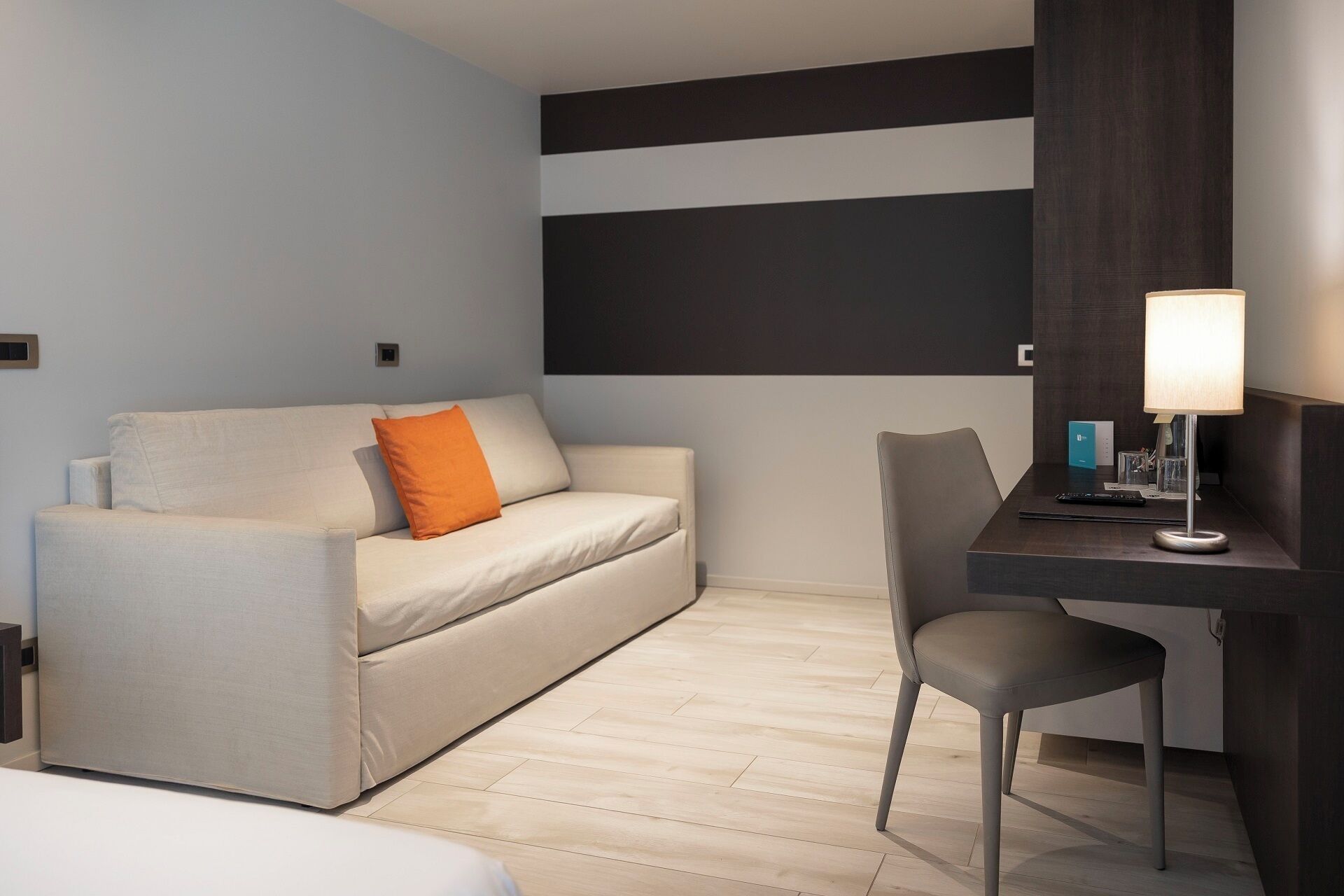Une chambre d’hôtel avec un canapé, un bureau, une chaise, une lampe et un mur orné d’un motif noir et blanc.